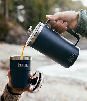 Pouring coffee from a Yeti insulated French press into a travel mug, showcasing durability and outdoor functionality.