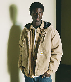 Man wearing a beige Carhartt WIP jacket layered over a shirt, highlighting rugged workwear-inspired style and craftsmanship.