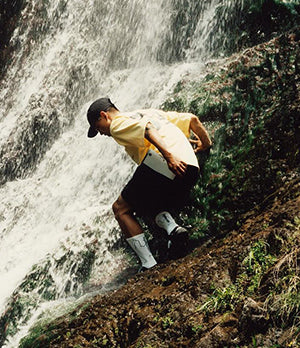 Man climbing near a waterfall wearing Goldwin outdoor gear, highlighting performance and style for adventurous activities.