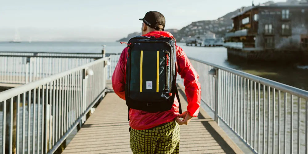 Man Walking Along a Pier Wearing a Red Topo Jacket and a Topo Backpack