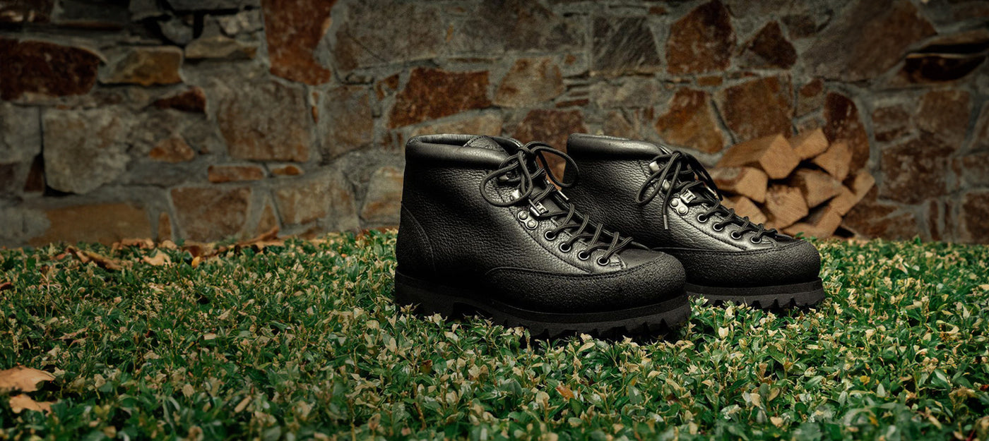 A pair of Paraboot leather boots on grass against a stone wall backdrop, showcasing their rugged design and craftsmanship.