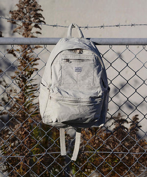 Light grey Porter Yoshida backpack hung on a wire fence, capturing the brand's sleek design and urban functionality in a street-style setting.