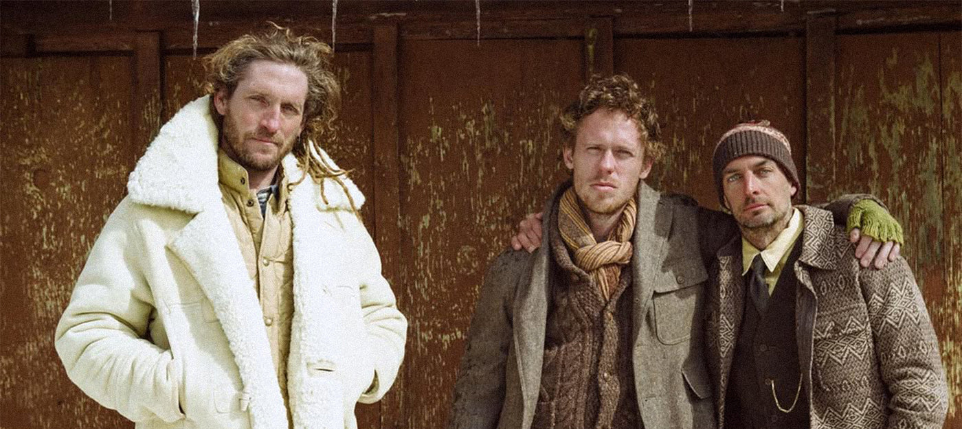 Three men wearing RRL by Ralph Lauren clothing standing together against an old wooden wall.
